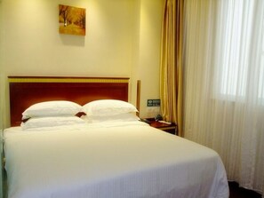 Una habitación de hotel con una cama grande, un cabecero de madera, una mesita de noche con un teléfono y un cuadro en la pared.