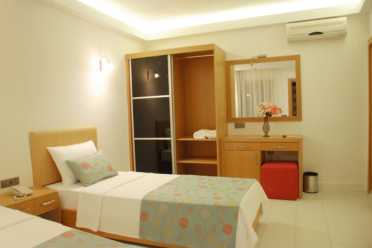 Habitación de hotel con dos camas, un armario, un escritorio, un espejo y un cubo de basura.