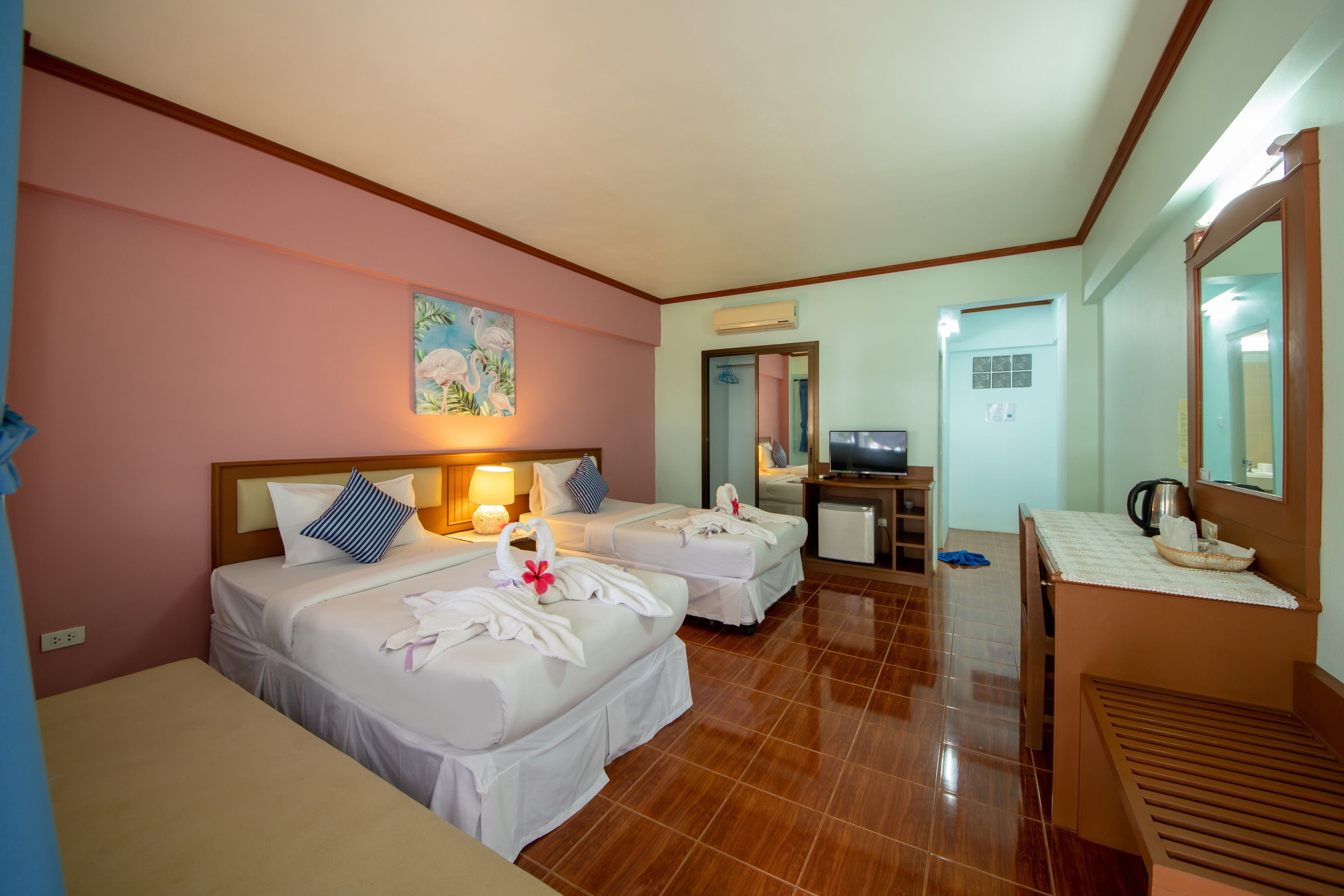 A hotel room with two beds, a desk, a TV, and a mirror.