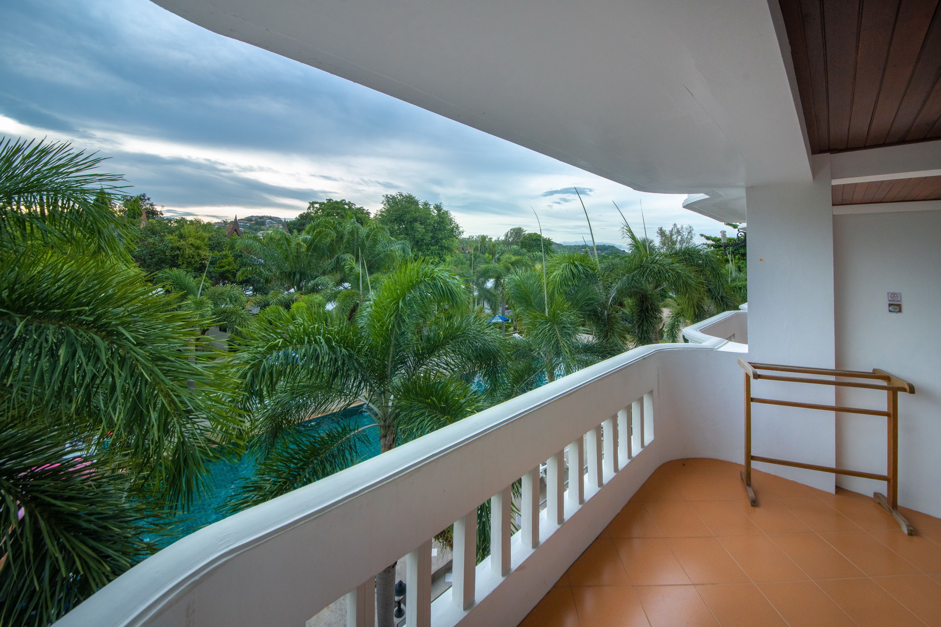 A balcony with a white railing, overlooking a lush green landscape with trees and a pool.