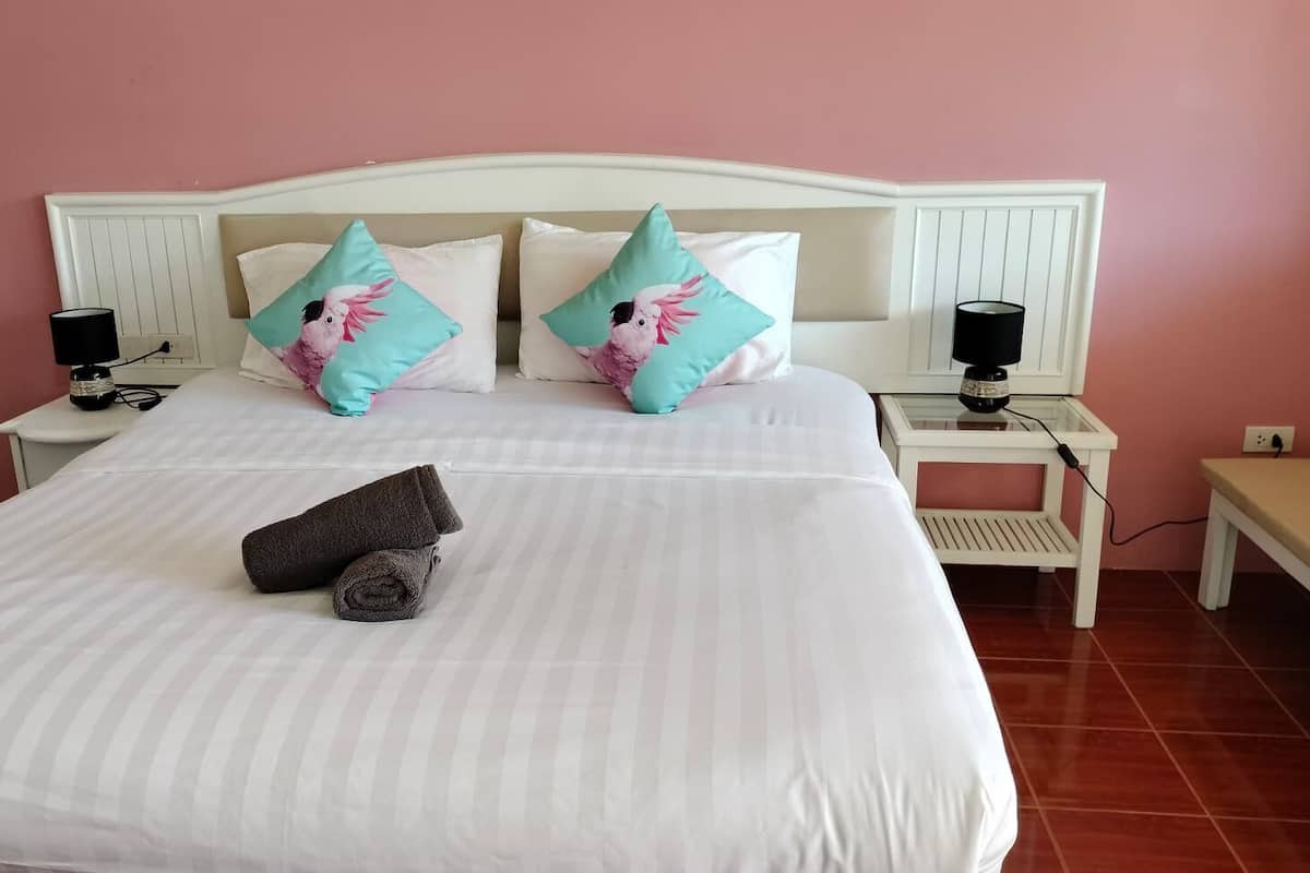A neatly made bed with striped bedding, two teal pillows with a parrot design, and two rolled towels.