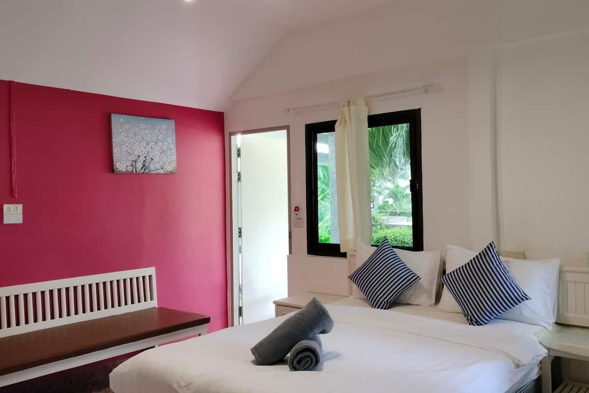 A bedroom with a bed, a bench, a window with curtains, and a painting on the wall.