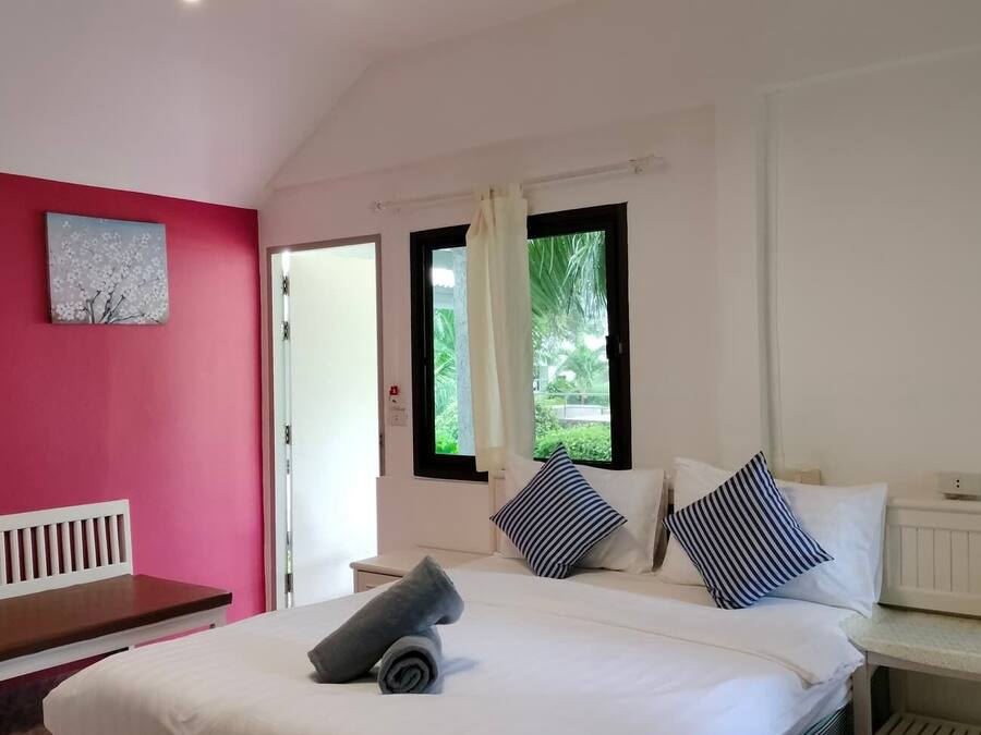 A bedroom with a bed, a bench, a window with curtains, and a painting on the wall.