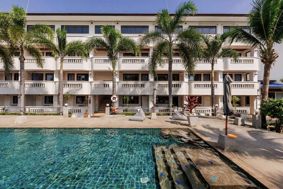 A hotel with a swimming pool, palm trees, and a multi-story building with balconies.