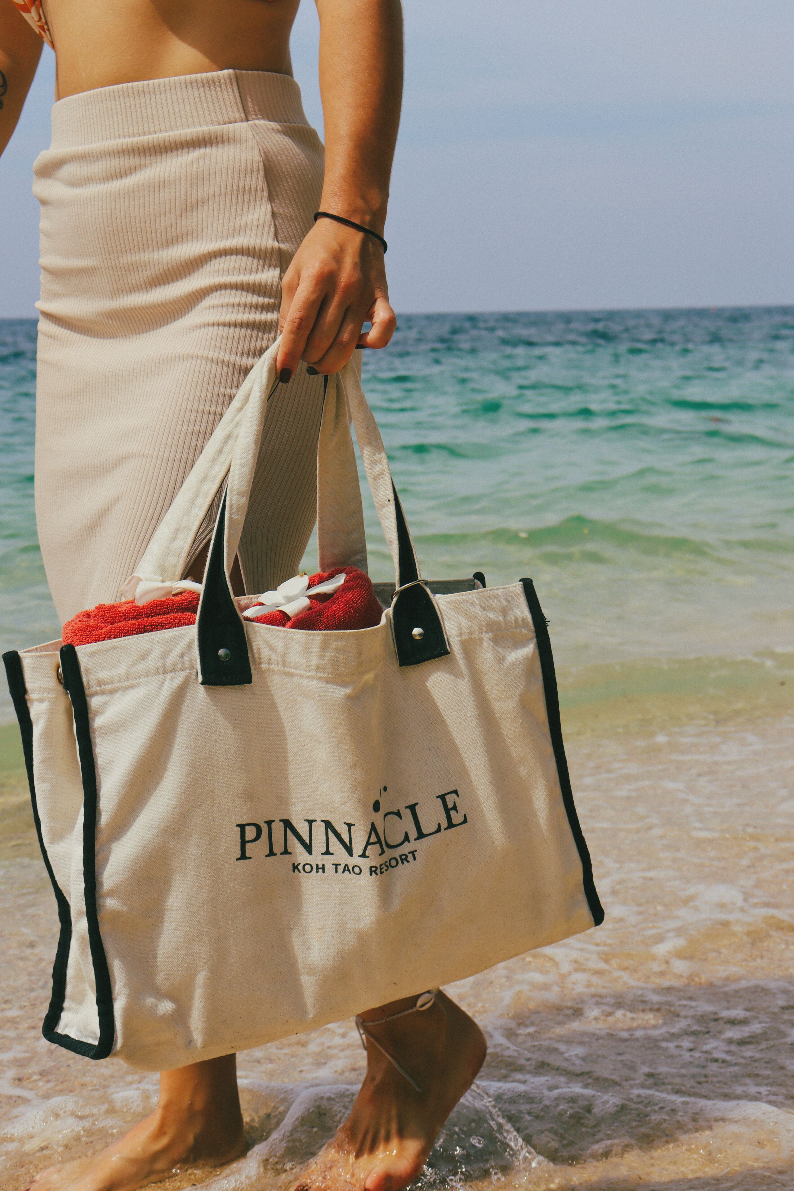 A person holding a beige bag with black straps and the word 'PINNACLE' on it.