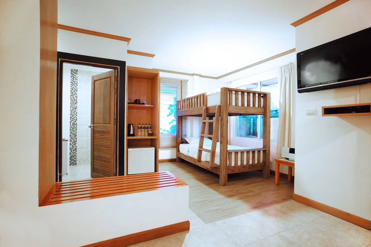 A room with a bunk bed, a TV mounted on the wall, a small table, and a wooden shelf with various items.