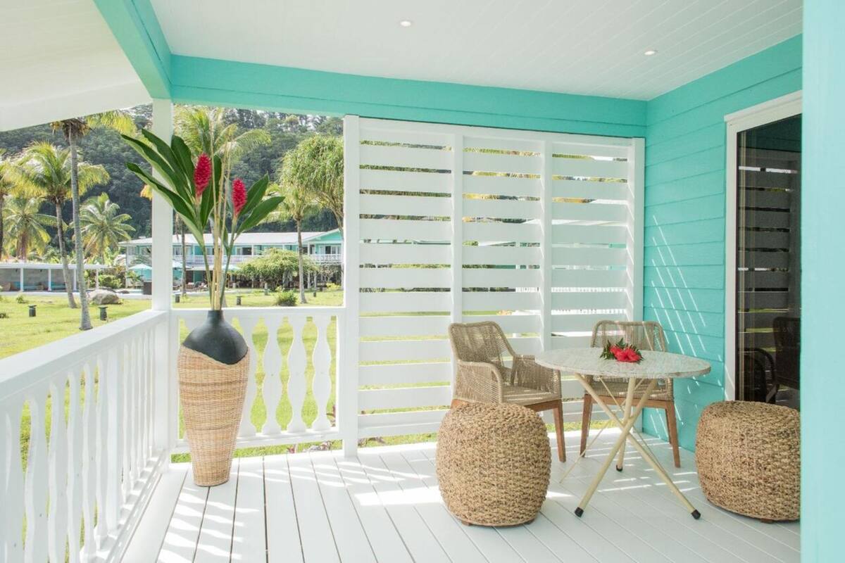 A covered outdoor seating area with a white railing, wicker furniture, and a view of a tropical landscape.