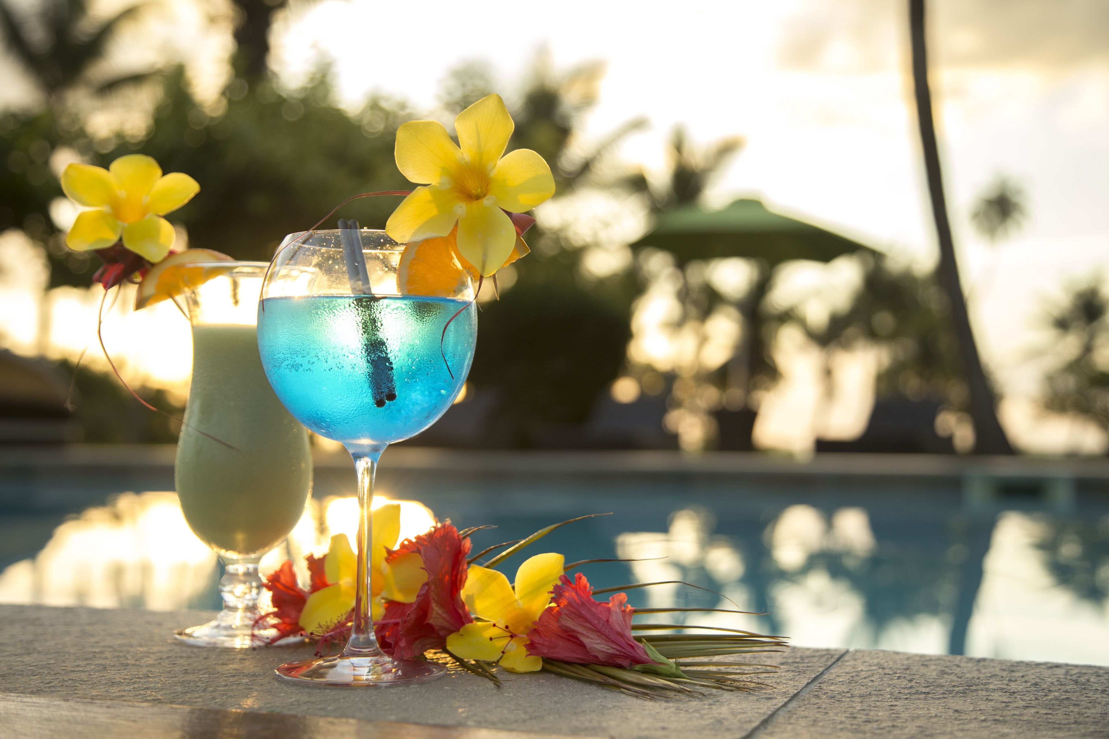 Zwei Cocktails mit tropischen Blumen auf einem Tisch am Pool.