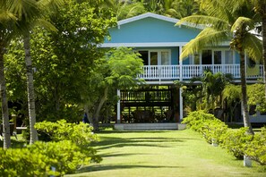A two-story house with a balcony, surrounded by lush greenery and palm trees.