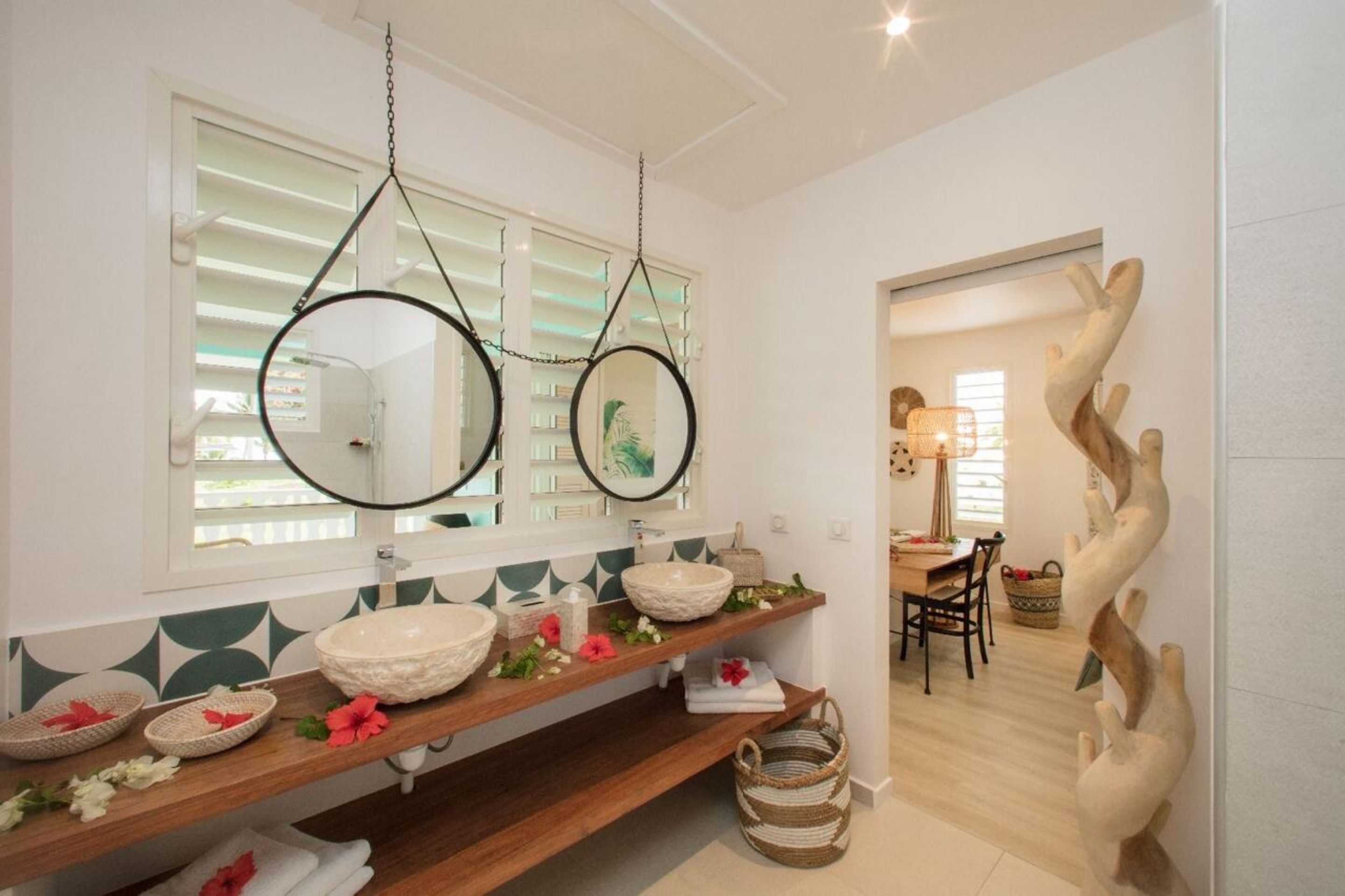 A bathroom with a wooden vanity, two round mirrors, and a decorative wall sculpture.