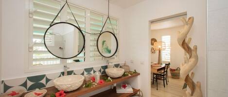 Un bagno con un mobile vanitario in legno, due specchi rotondi e una scultura decorativa a parete.