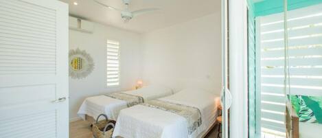 A bedroom with two beds, a ceiling fan, and a view of the outside through large windows.