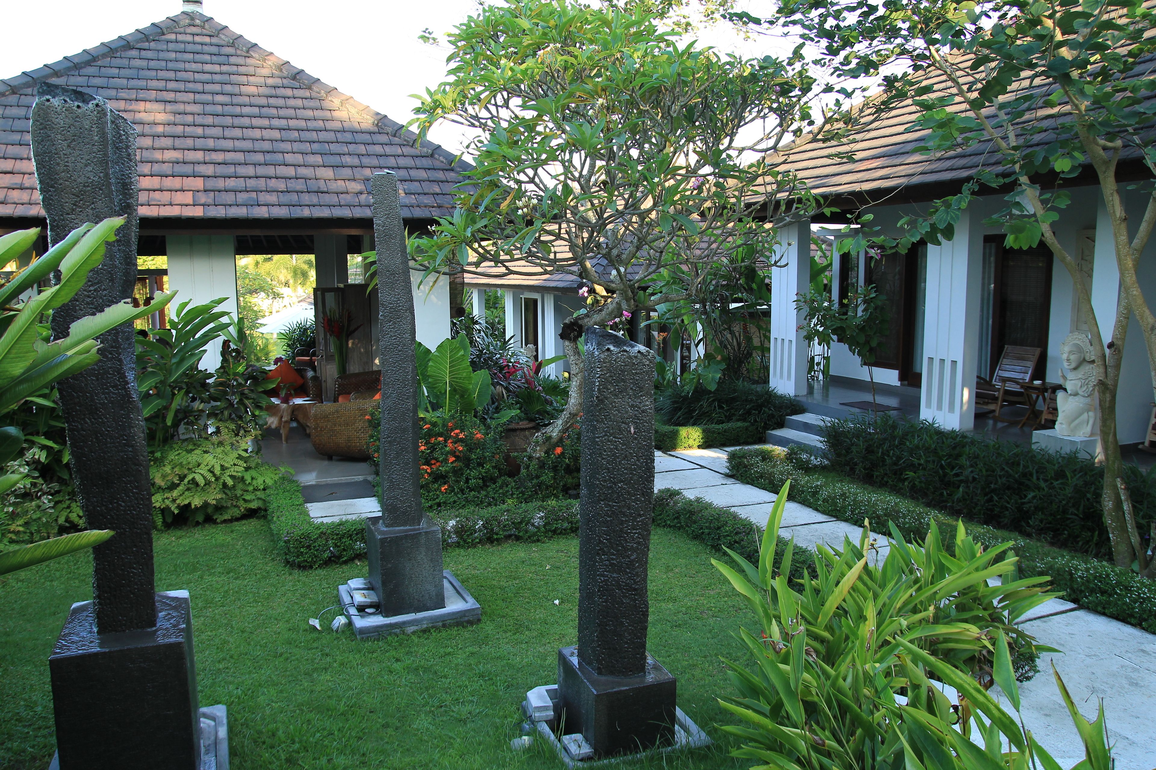 A garden with stone pillars, a tiled roof structure, and lush greenery.