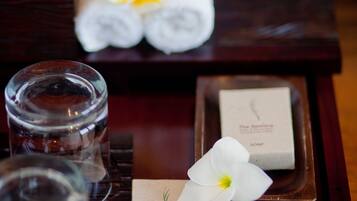 Una bandeja de madera con toallas enrolladas con cuidado, un vaso de agua, una flor blanca y pequeños paquetes de jabón etiquetados como "The Samara".