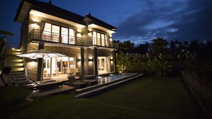 A two-story house with a swimming pool, outdoor seating, and a well-lit patio area. - The Samara (Ubud)