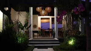 A well-lit entrance with a staircase leading to a dining area, surrounded by lush greenery and tropical plants. - The Samara (Ubud)