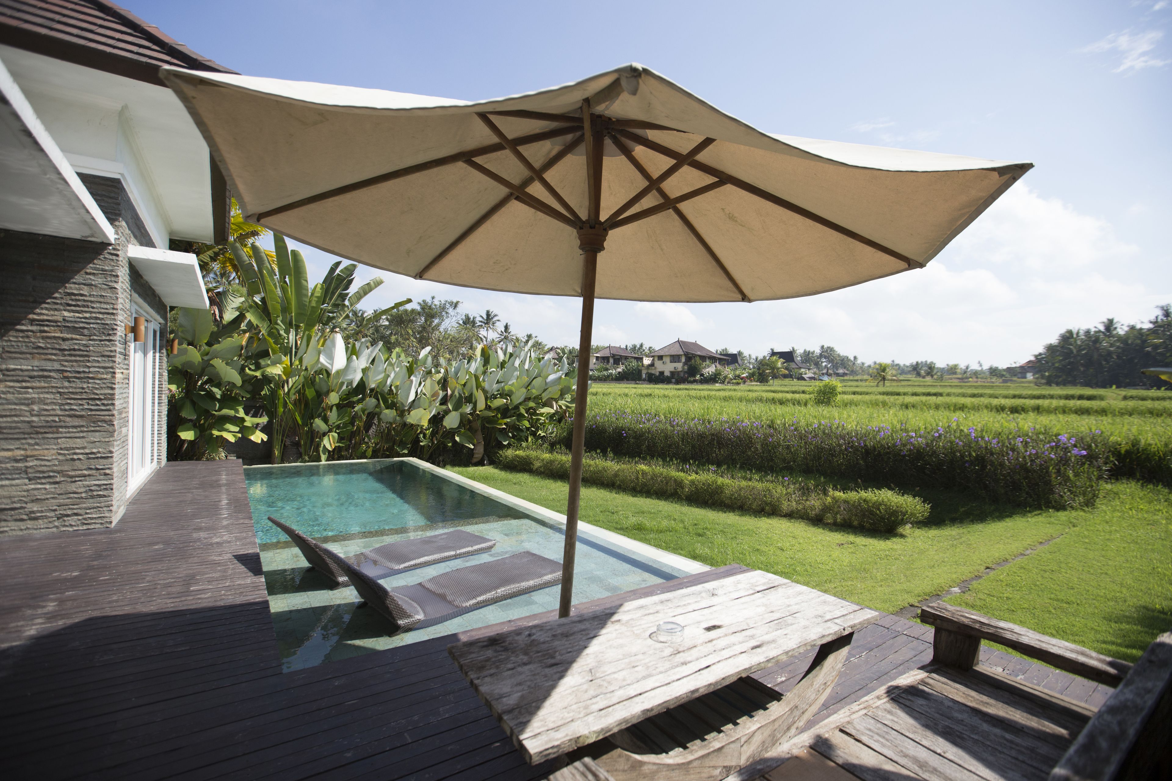 A pool area with a wooden deck, lounge chairs, and a large umbrella.