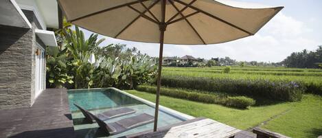 A pool area with a wooden deck, lounge chairs, and a large umbrella.