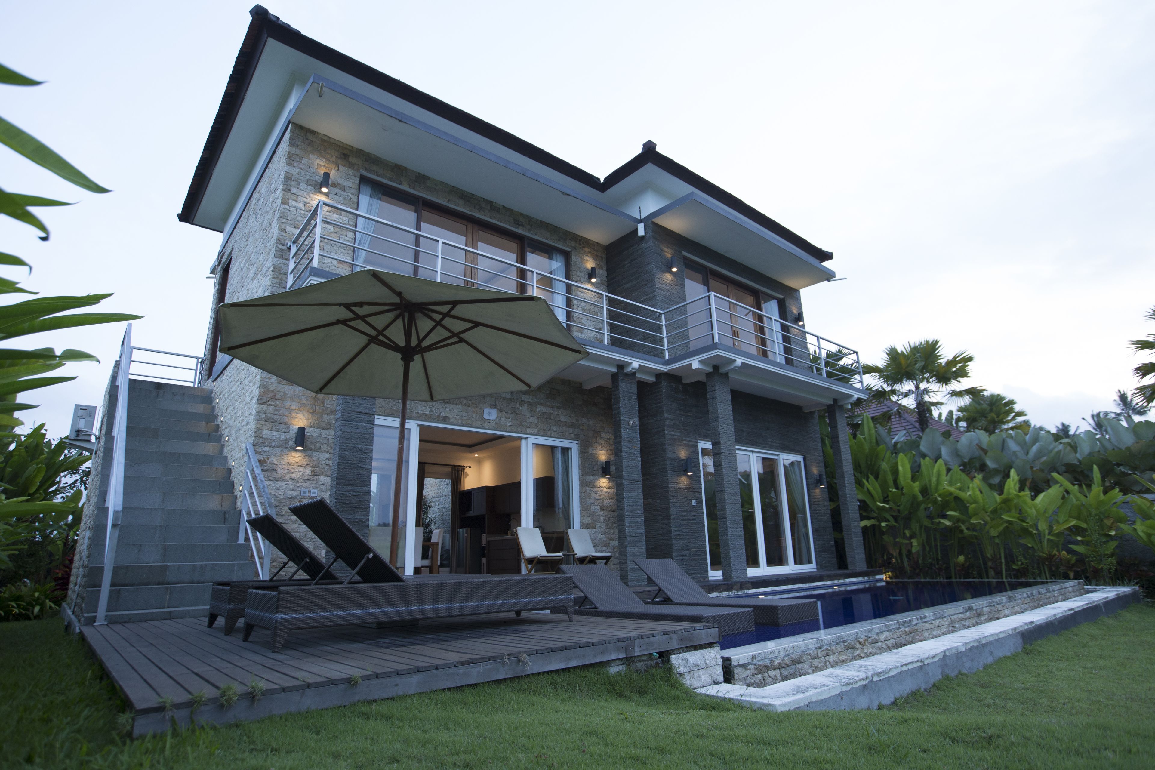 Una casa moderna de dos pisos con balcón, mobiliario exterior y piscina.