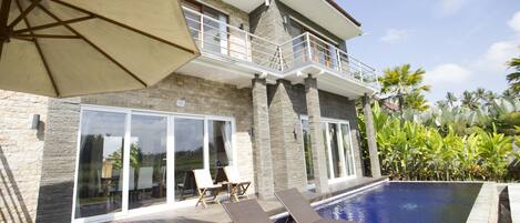 Una casa moderna con piscina, balcón y zona de patio con sillones de descanso.