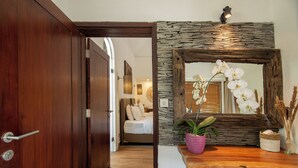 A hallway with a wooden door, a stone wall, and a mirror reflecting an orchid. - The Samara (Ubud)