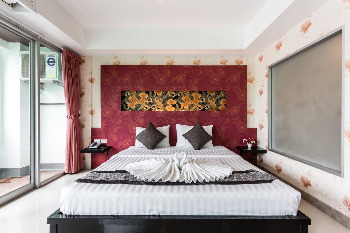 A hotel room with a large bed, a decorative headboard, a window with a view, and a sliding door to the outside.