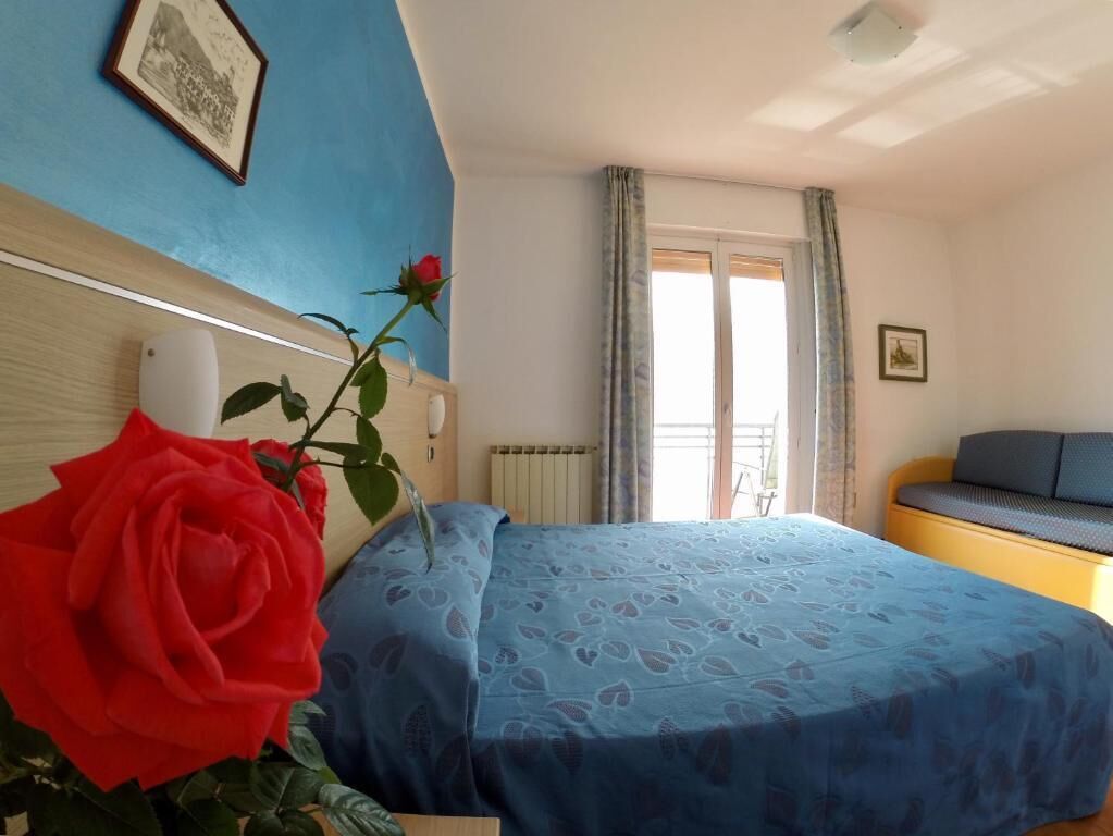 Un dormitorio con cama, mesita de noche, ventana con cortinas e imagen enmarcada en la pared.
