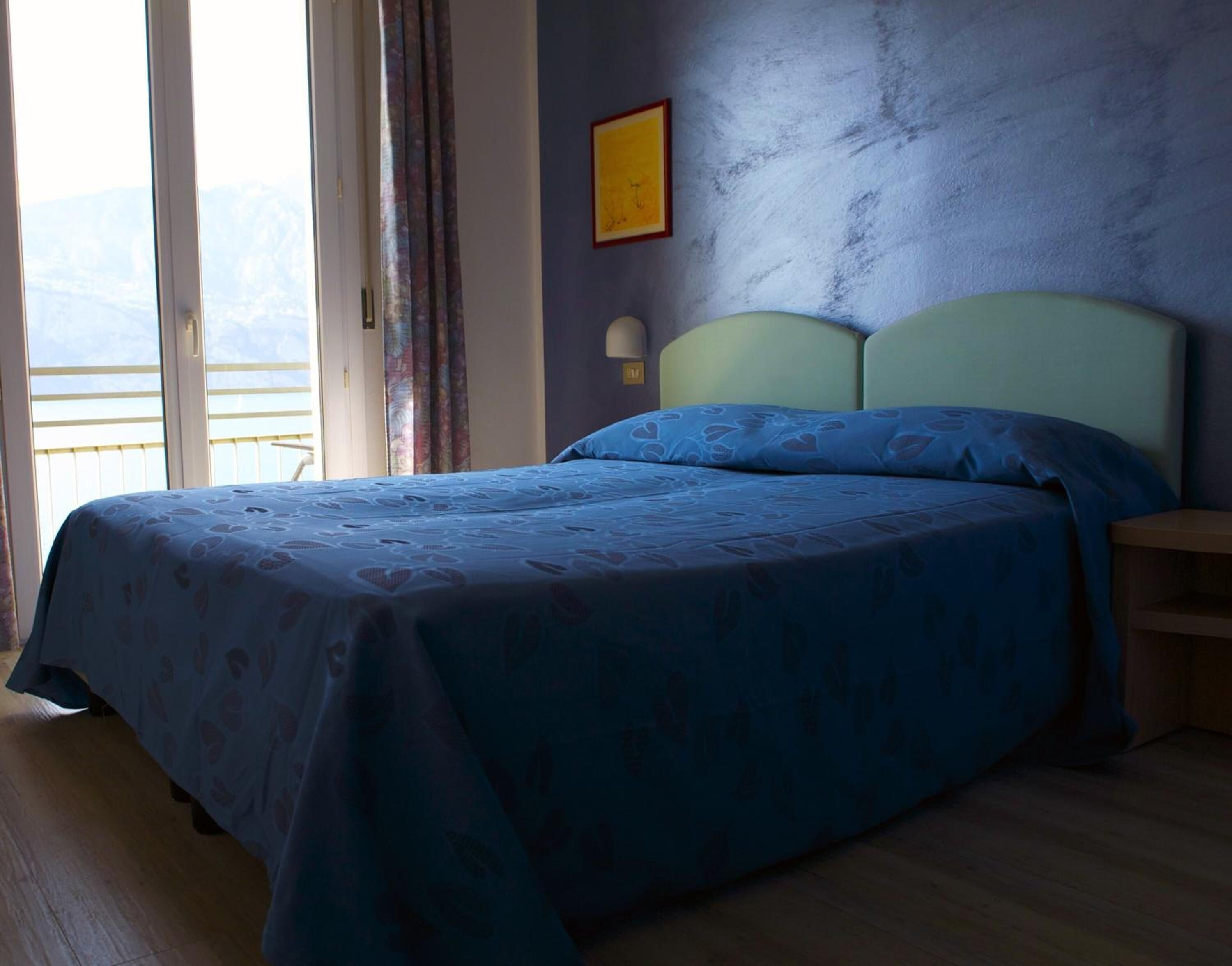 Une chambre à coucher avec un lit, une table de chevet, une lampe fixée au mur et une fenêtre avec des rideaux.