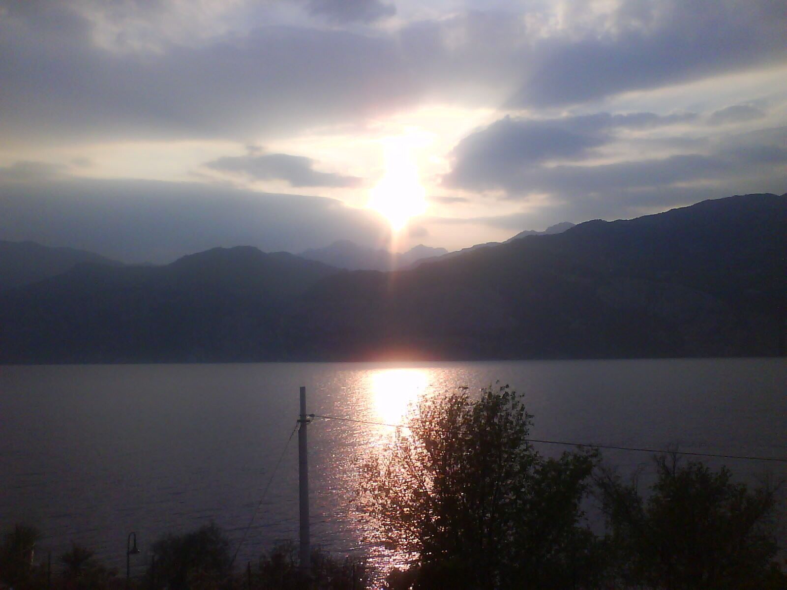 Ein See mit Bergen im Hintergrund und der Sonne, die über dem Wasser aufgeht oder untergeht.