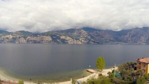 A coastal view with a clear sky, mountains in the background, and a beach with a few trees and buildings. - Villa Edera (Malcesine)
