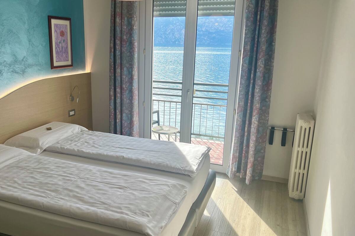 Habitación de hotel con dos camas, vista al mar, un cuadro enmarcado en la pared y un radiador.