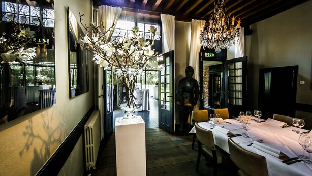 A restaurant interior with a long table set for dining, a vase with flowers, and a statue in the background. - Fletcher Landgoedhotel Renesse (Renesse)
