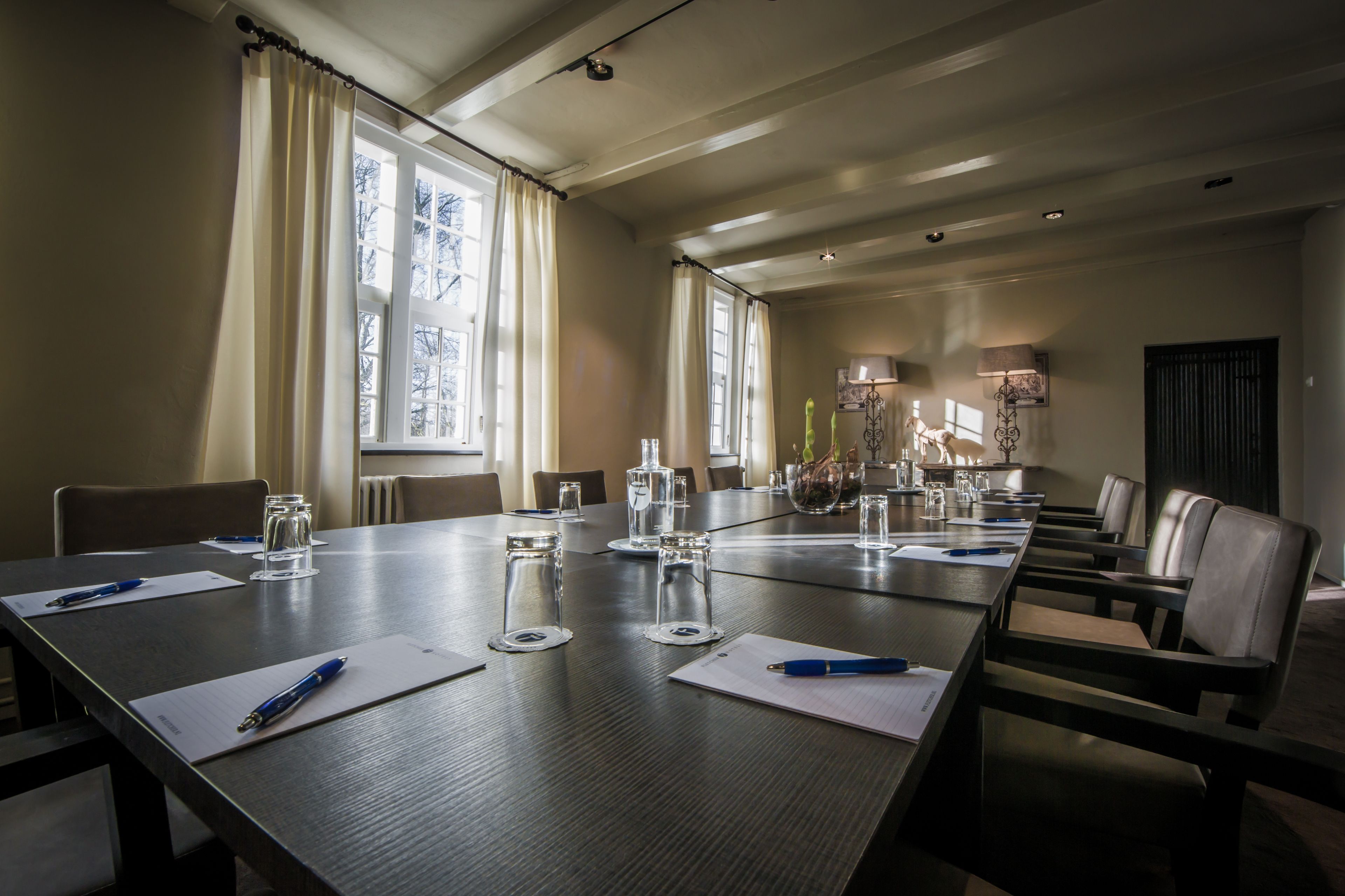 A conference room with a long table, chairs, and a window with curtains.