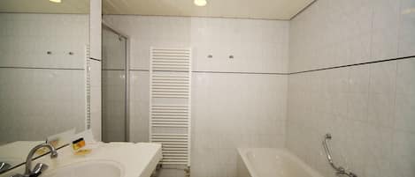 Un baño con lavamanos, espejo, bañera y toallero.