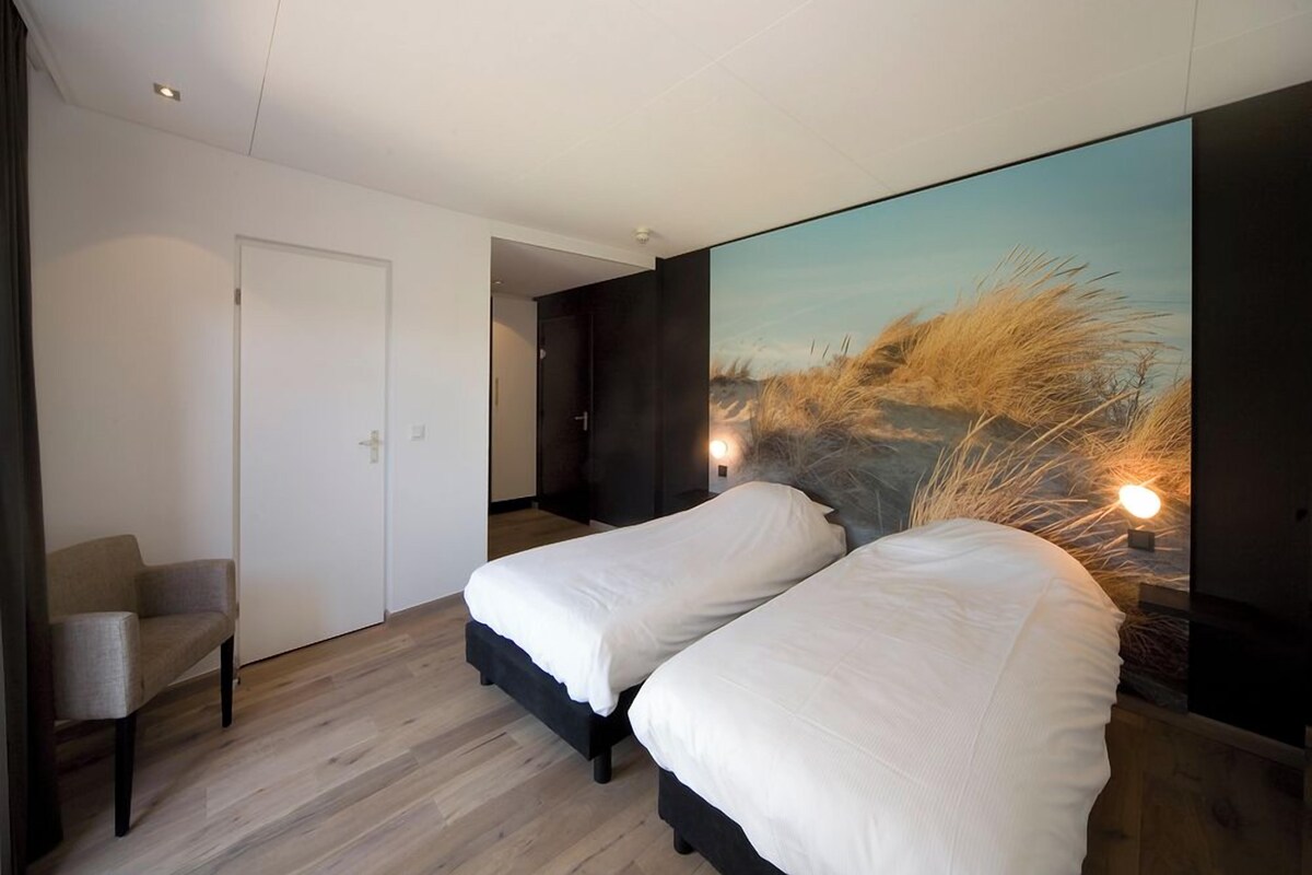 A bedroom with two beds, a chair, a door, and a large wall mural.