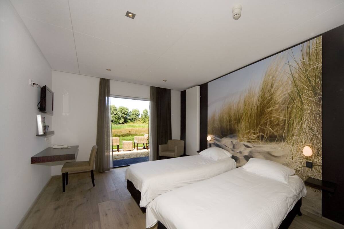 Habitació d'hotel moderna amb dos llits, un escriptori amb cadira, un televisor i una finestra gran que ofereix vistes a l'exterior.