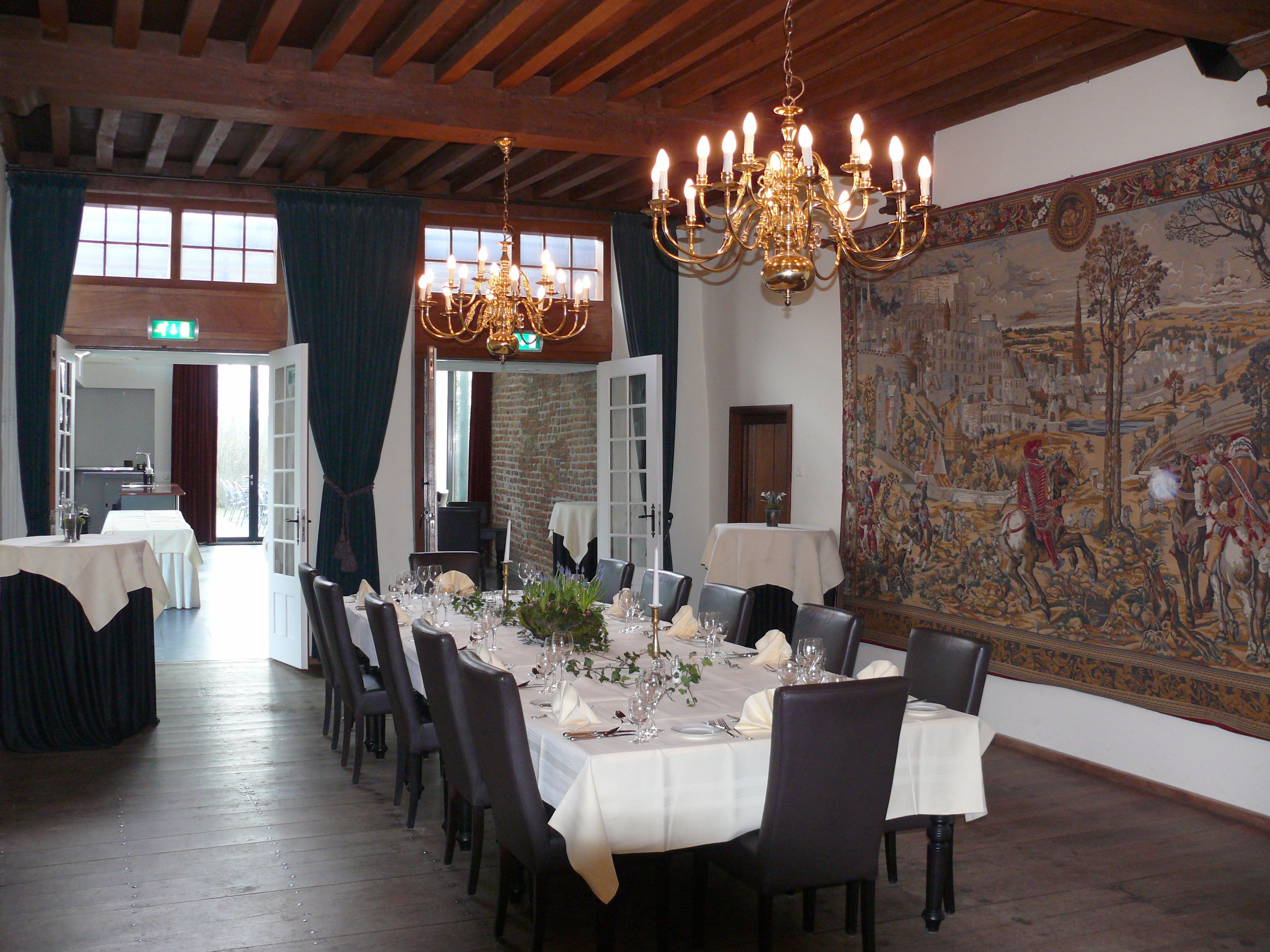 A dining room with a long table set for a meal, a chandelier, and a large historical painting on the wall.