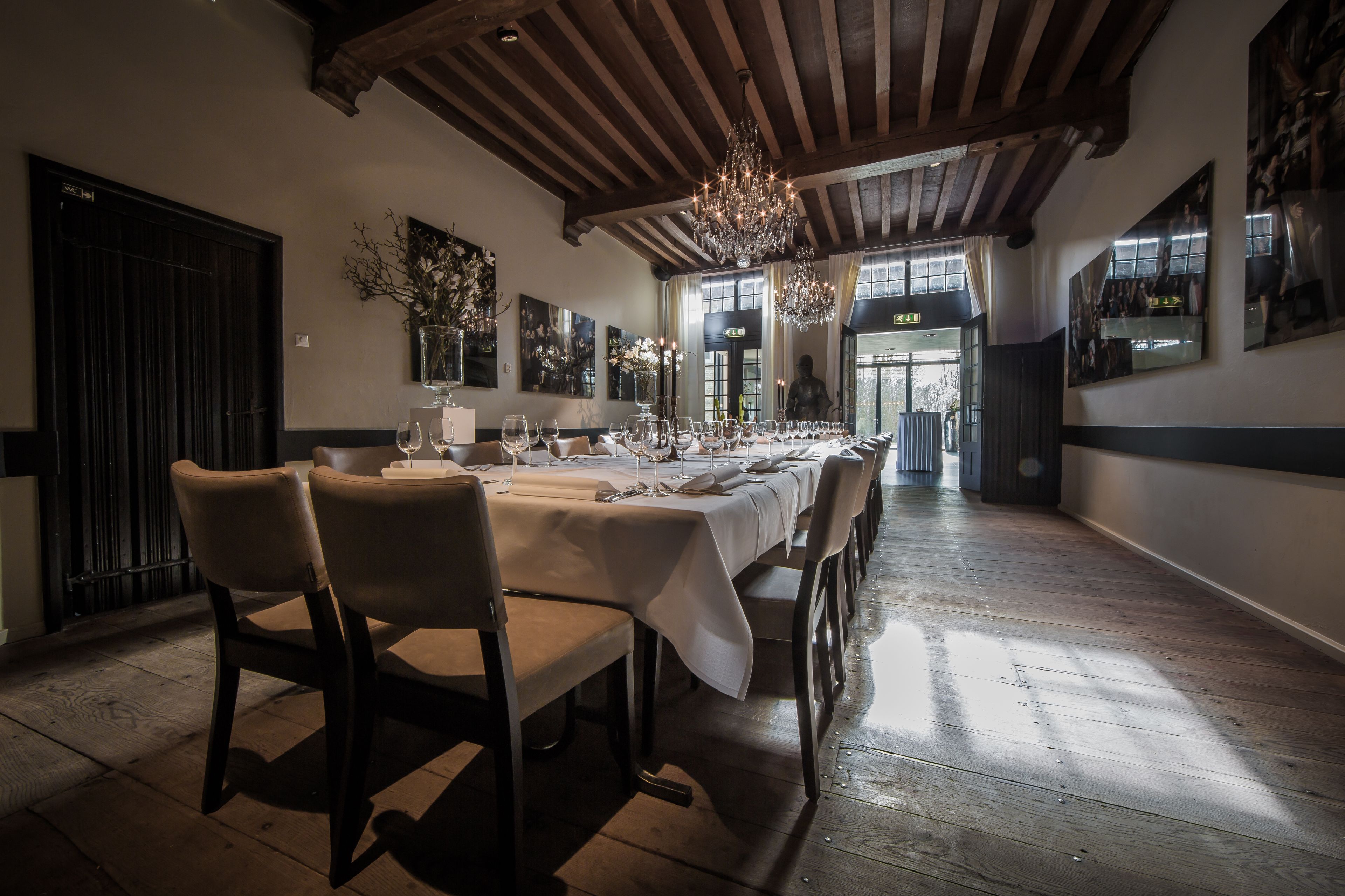 A dining area with a long table set for a meal, wooden beams on the ceiling, and artwork on the walls.