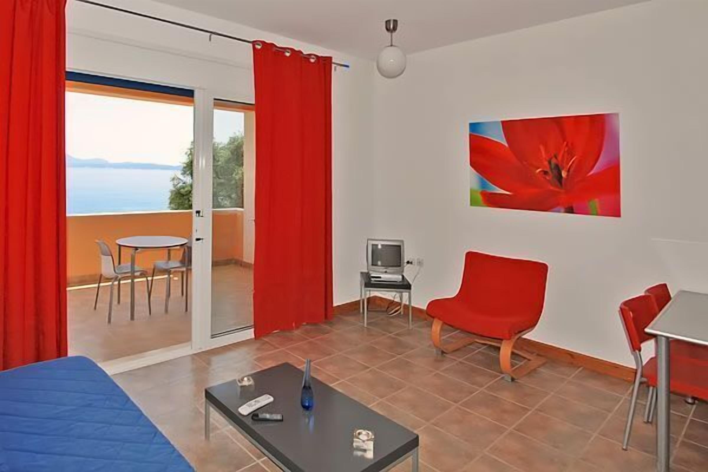 Una stanza con un letto, un tavolo con un vaso, una TV e una sedia rossa.