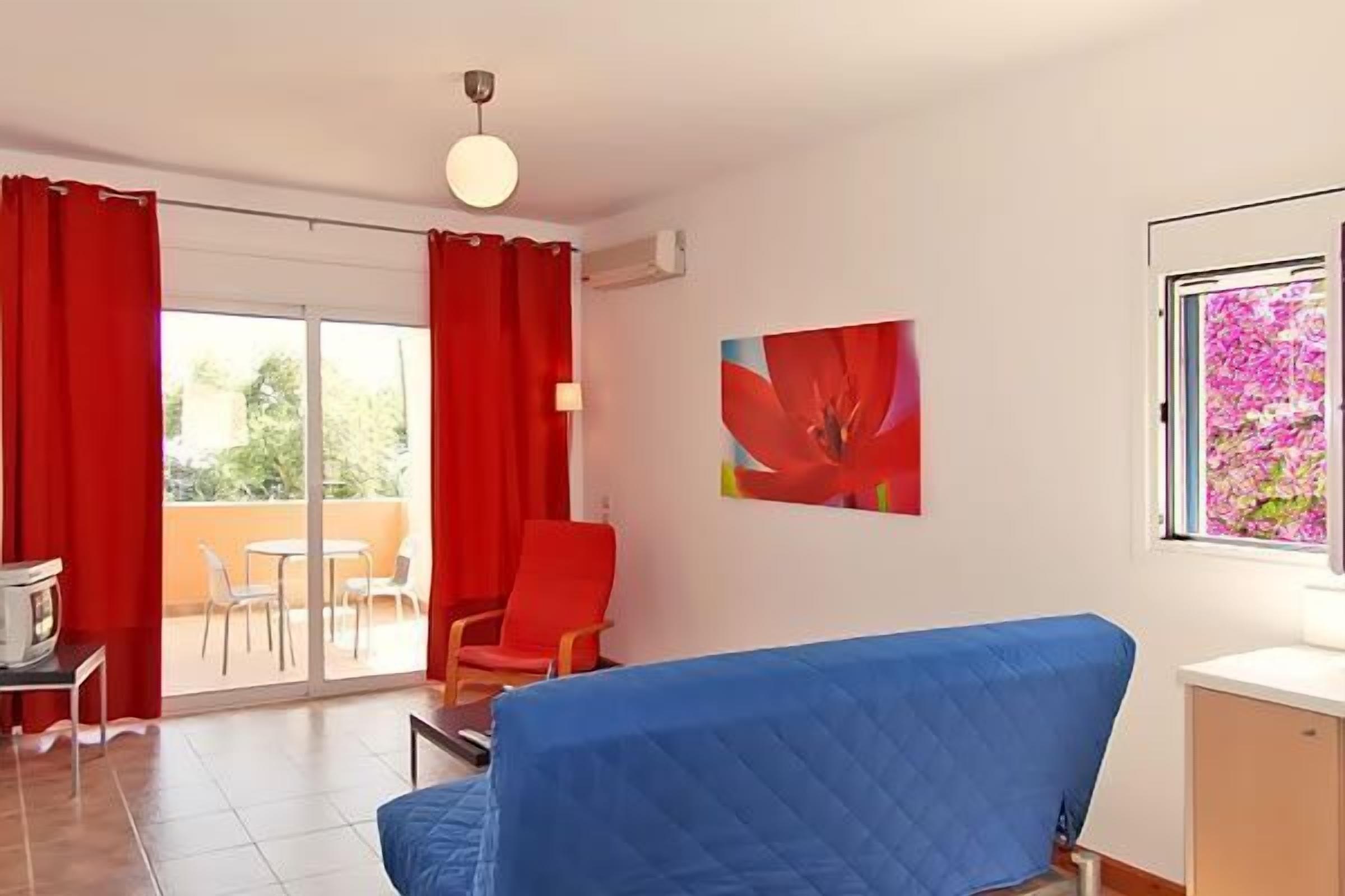 Ein Zimmer mit einem blauen Sofa, einem roten Sessel, einem Tisch mit Lampe und einem Bild an der Wand.