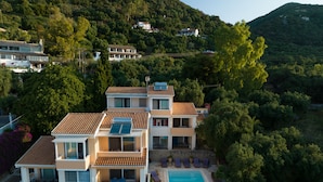 A multi-story residential building with a swimming pool, surrounded by lush greenery and hills.