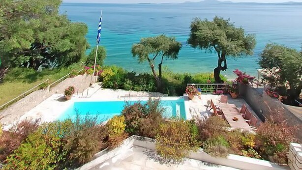 A pool area with a flag, surrounded by trees and a view of the sea.