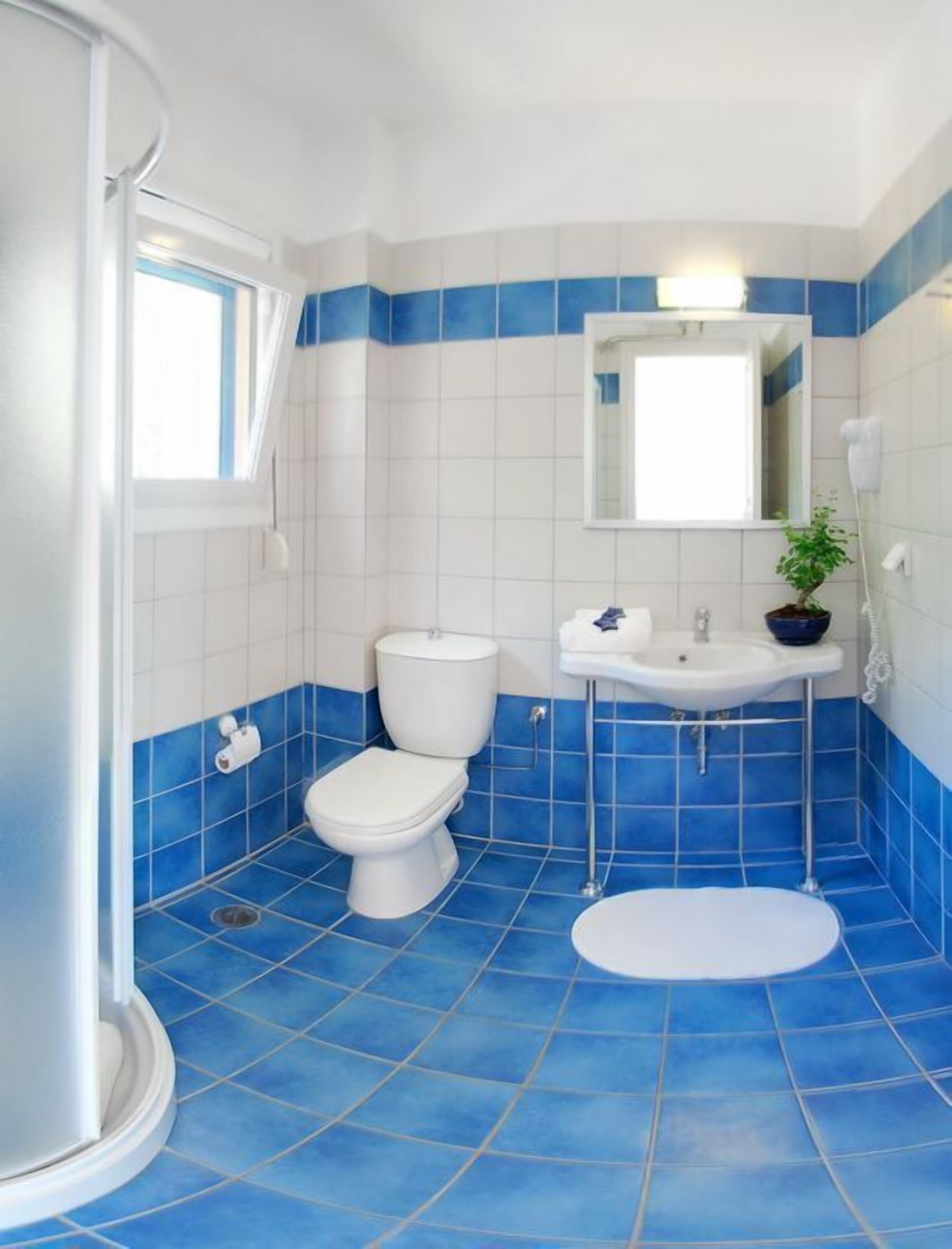 A bathroom with a toilet, sink, and bidet, featuring blue and white tiles and a potted plant.