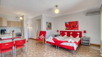 A modern hotel room with a red and white color scheme, a bed, a desk with a chair, a small kitchen area, and a bathroom.