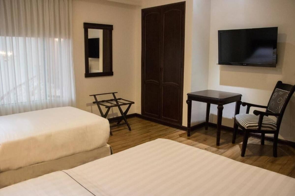 Una habitación de hotel con dos camas, una mesita, una silla, un televisor y un armario.