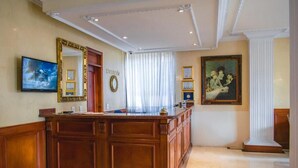 A spacious lobby with a large wooden reception desk, a television mounted on the wall, and framed certificates on the wall. - Hotel Castilla Real (Pereira)