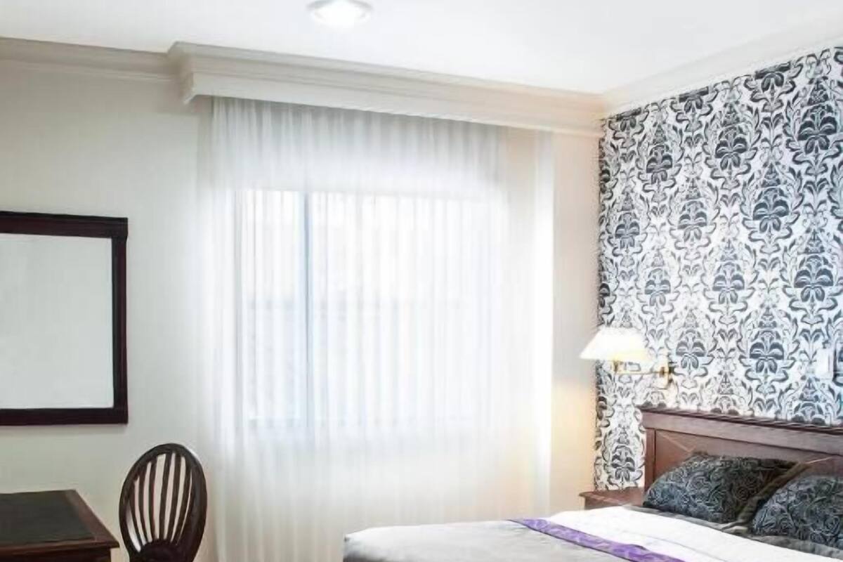 Habitación de hotel con cama, escritorio, silla, ventana con cortinas y pared con diseño.