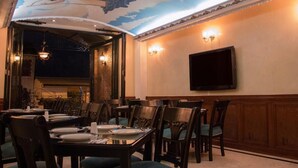 A dining area with tables and chairs, a flat-screen TV mounted on the wall, and a mural on the ceiling. - Hotel Castilla Real (Pereira)