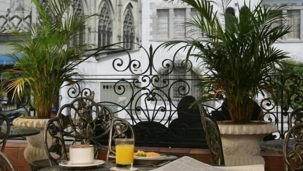 An outdoor patio with wrought iron furniture, a table with a cake and a glass of orange juice, and potted plants. - Hotel Castilla Real (Pereira)