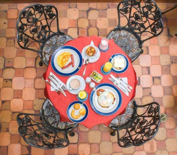 A round table with a red tablecloth, surrounded by four black metal chairs with intricate designs.